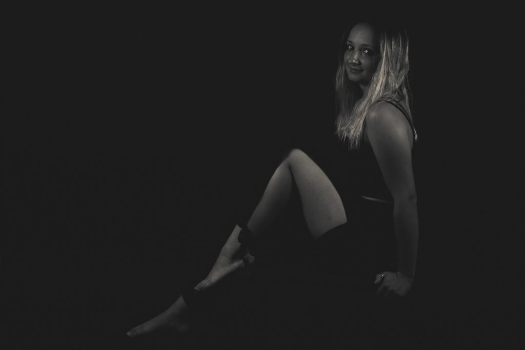 Océane assise sur fond sombre, portrait en noir et blanc